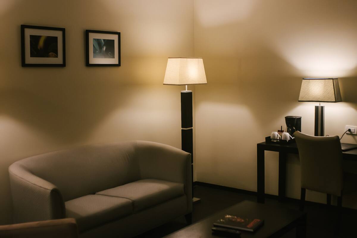 A dimly lit room with a sofa, two framed pictures on the wall, and two standing lamps.