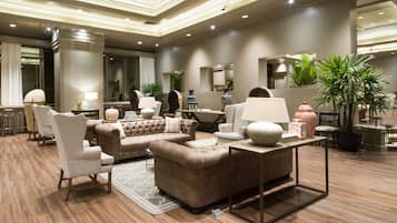 A spacious lobby with a central seating area featuring sofas and armchairs, a coffee table, and a side table with a lamp.