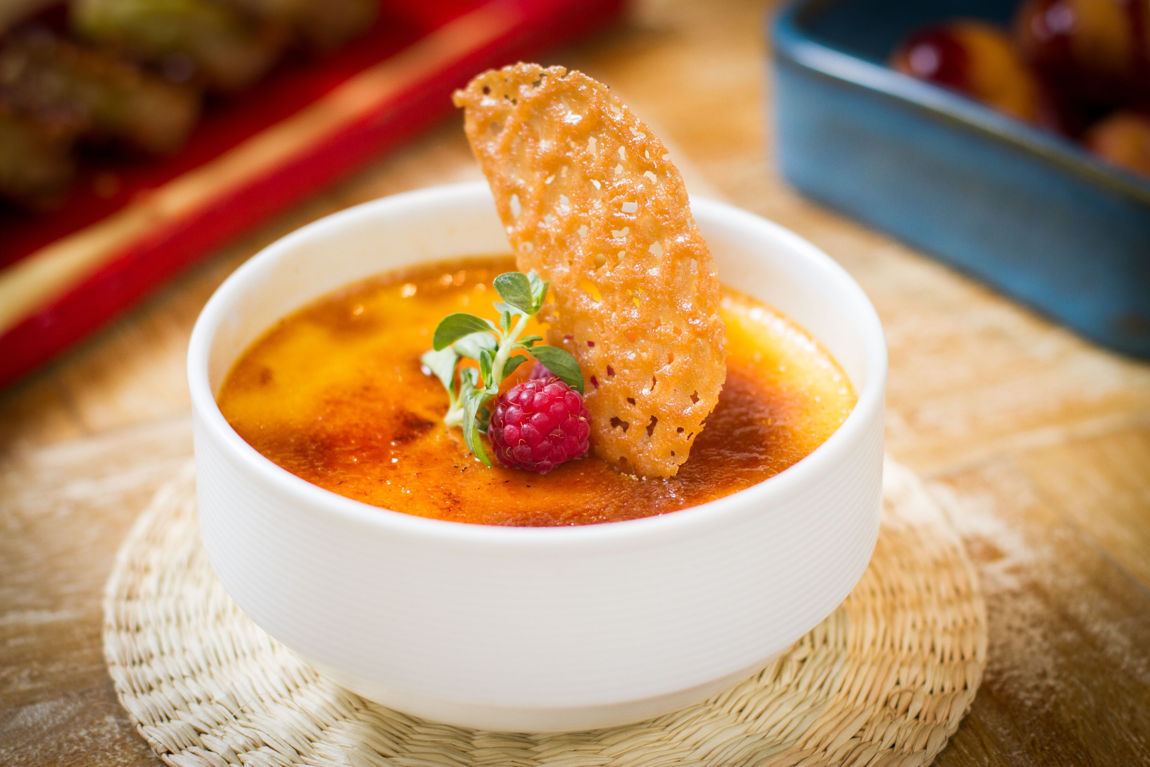 Un bol de soupe sur lequel on a posé une tranche de pain, le tout garni d’une framboise et d’une branche d’herbe aromatique.