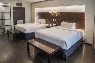 Habitación de hotel con dos camas, un banco, una mesita de noche y una lámpara fijada a la pared.