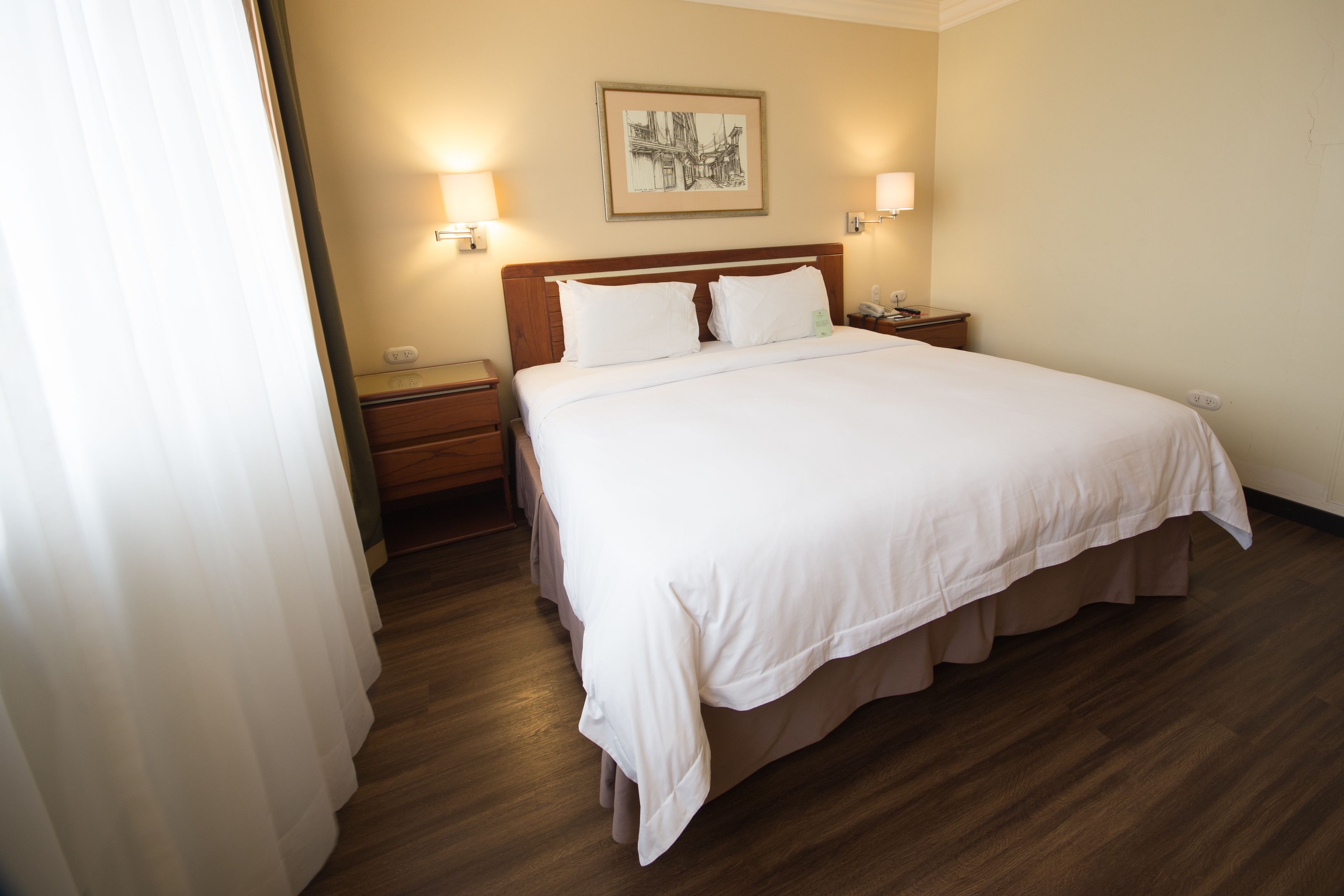 Una habitación de hotel con una cama grande, cabecera de madera, dos mesitas de noche y un velador.