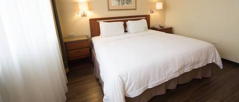 Una habitación de hotel con una cama grande, cabecera de madera, dos mesitas de noche y un velador.