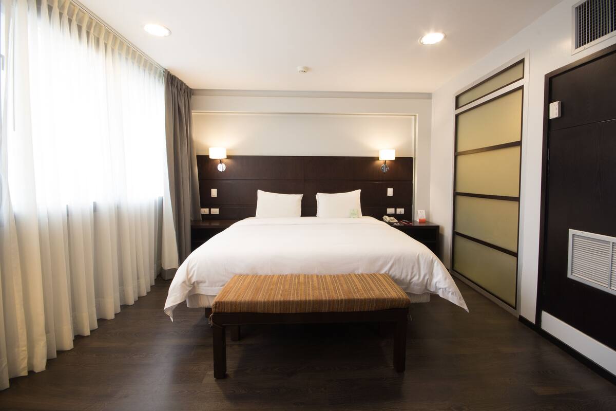 A hotel room with a large bed, bedside lamps, a bench, and a sliding door.