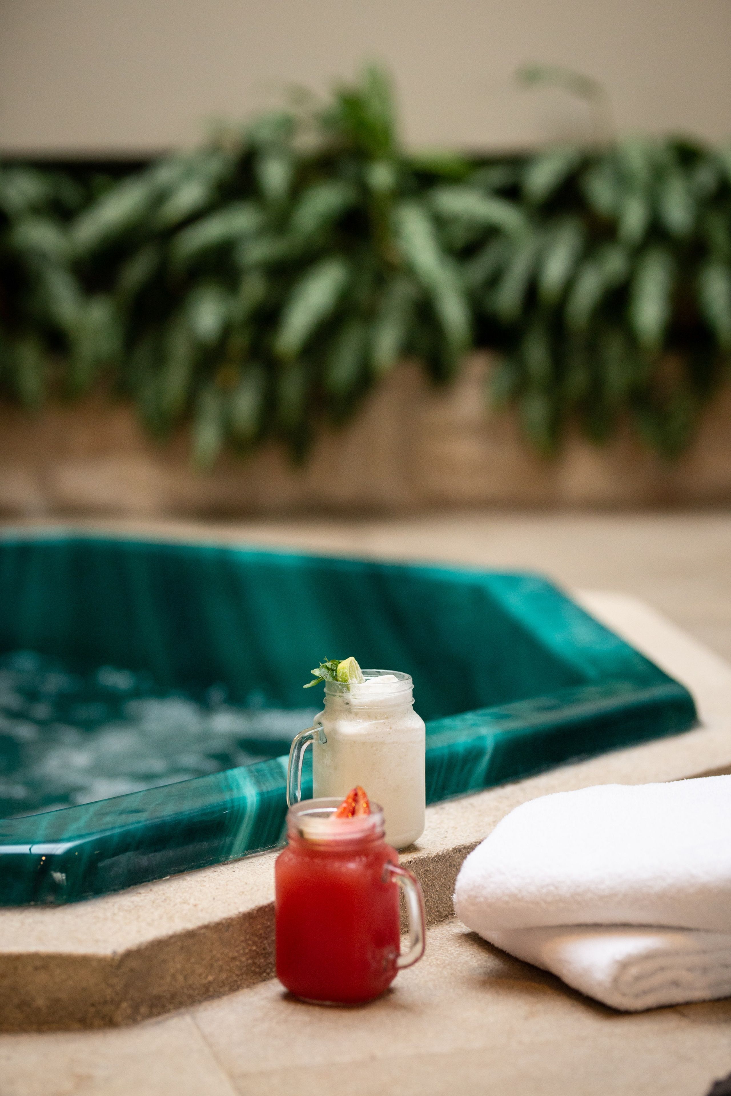 A pool area with a glass jar and a bottle of drink, a towel, and a plant in the background.