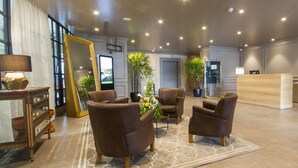 A modern hotel lobby with leather armchairs, a reception desk, and a large mirror. - Unipark by Oro Verde Hotels (Guayaquil)