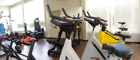 Un gimnasio con equipo de ejercicio, un televisor en la pared y ventanas amplias.