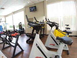 Un gimnasio con equipo de ejercicio, un televisor en la pared y ventanas amplias.