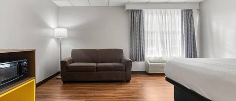 Hotelkamer met een bed, een sofa, een lamp, een magnetron en een raam met gordijnen.