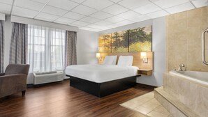 Une chambre d’hôtel avec un grand lit, un coin salon avec un fauteuil, une grande fenêtre avec des rideaux, un téléviseur fixé au mur et une baignoire.