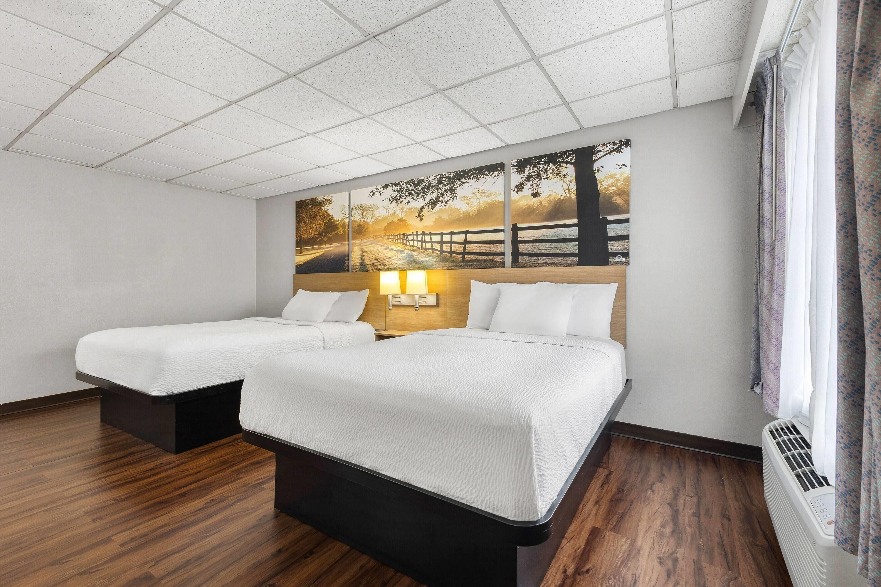 Habitación de hotel con dos camas, un mural grande en la pared, suelo de madera y una ventana con cortinas.