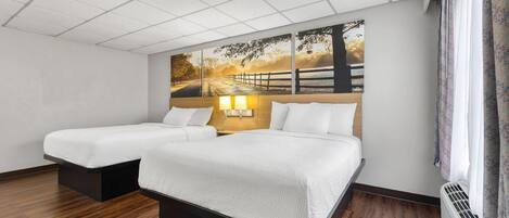 Habitación de hotel con dos camas, un mural grande en la pared, suelo de madera y una ventana con cortinas.
