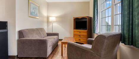Una sala de estar con sofá, sillón, mesa de madera, mueble para televisión y lámpara.