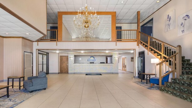 Un hall d’entrée spacieux avec un comptoir d’accueil, un lustre, un escalier et un fauteuil bleu.