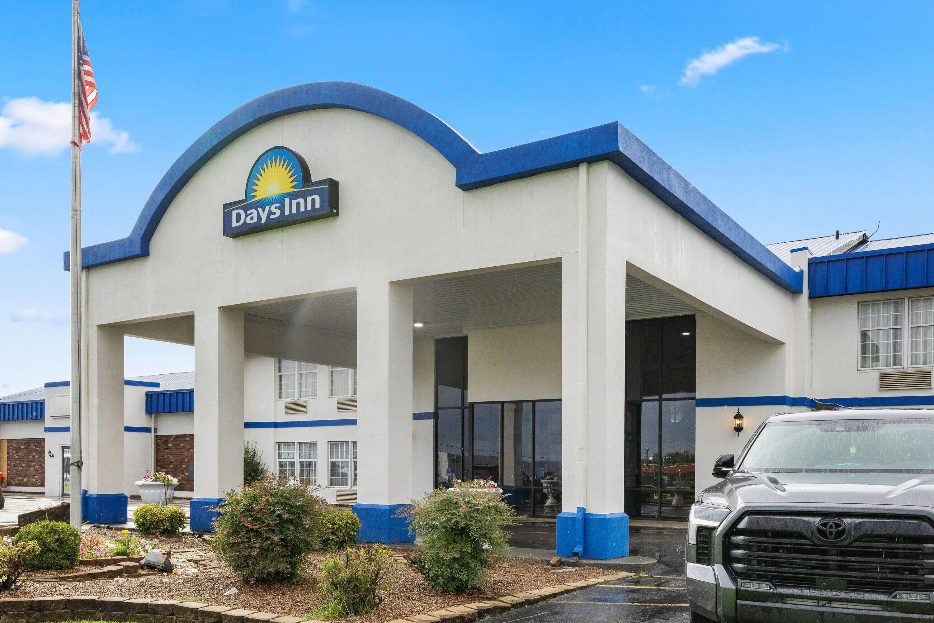 A Days Inn with a prominent entrance, a flagpole with an American flag, and a parking area with a vehicle.