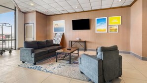 Un hall d’entrée moderne avec un canapé gris, des fauteuils, une table basse et un téléviseur à écran plat fixé au mur.