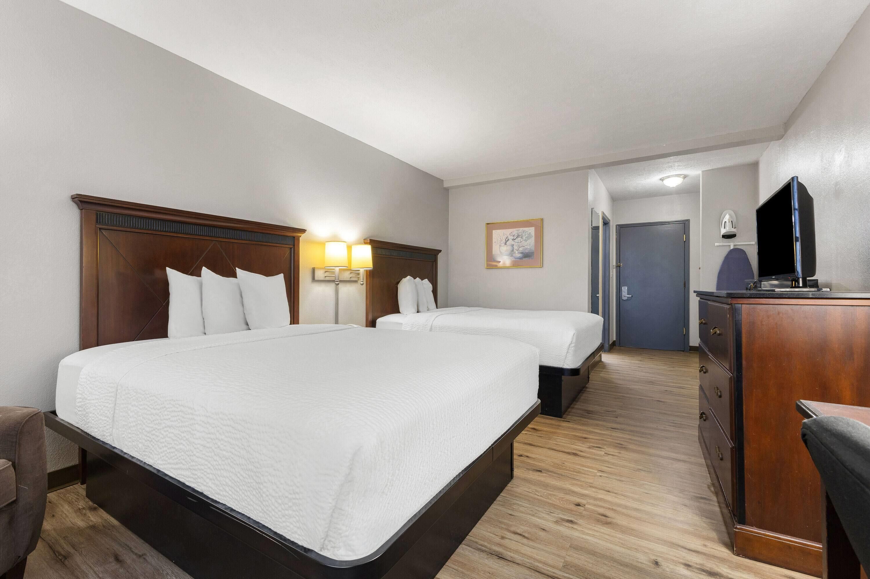Una habitación de hotel con dos camas individuales, un cabecero de madera, lámparas de noche, un televisor de pantalla plana, un aparador y una puerta que da a otra habitación.