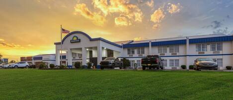 A Days Inn with a flat roof, a flag, and a parking lot with several cars.