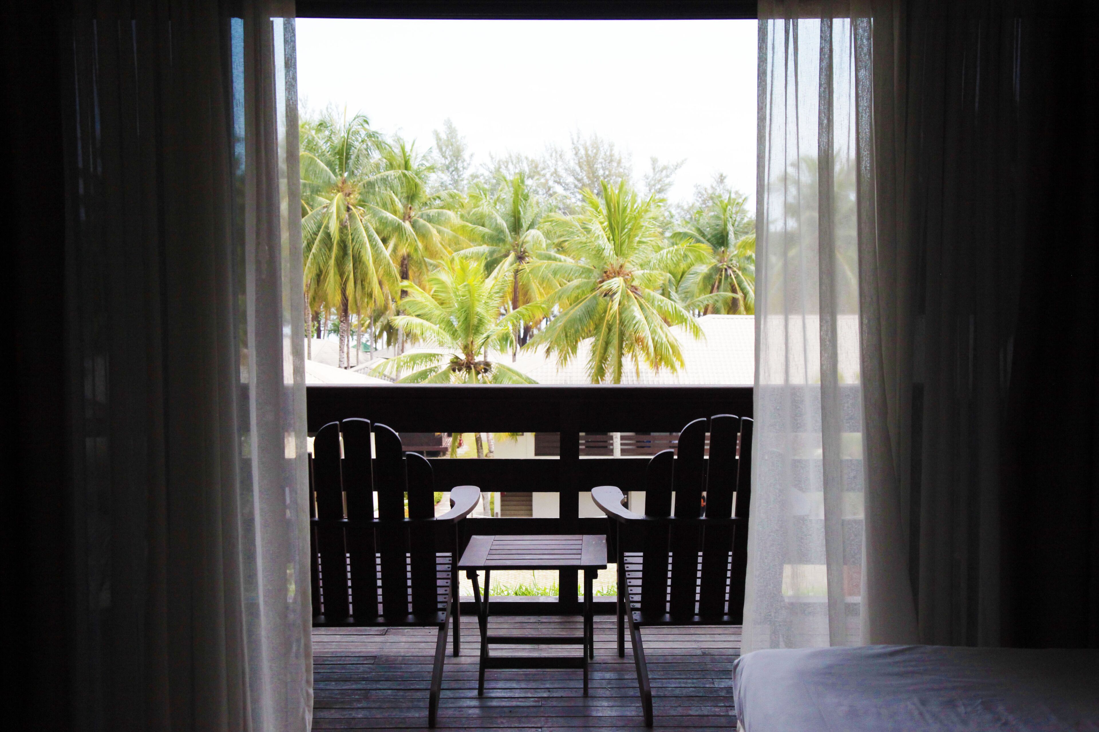 Un balcón con mesa y sillas de madera, con vistas a una zona bordeada de palmeras.