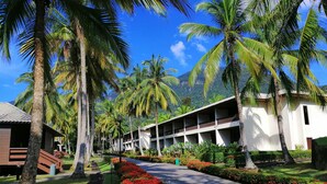 Un resort con un largo pasillo bordeado de palmeras y flores rojas, que conduce a un edificio con varios balcones.