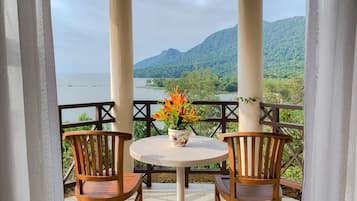 Relax in a serene outdoor seating area with a round table and two chairs, surrounded by lush green hills and a body of water.