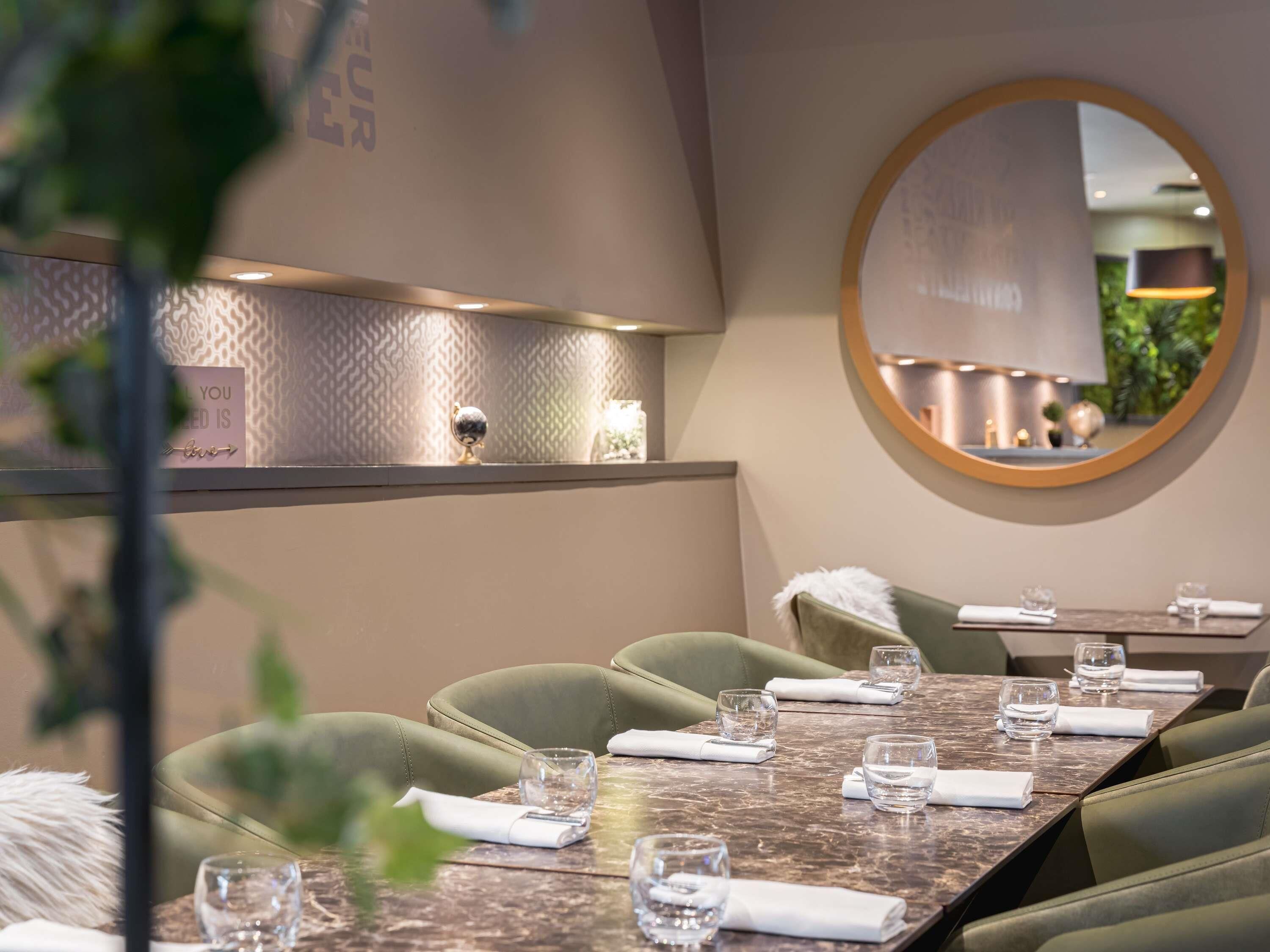 Un restaurante con una mesa de mármol, sillas tapizadas en verde y un espejo redondo en la pared.