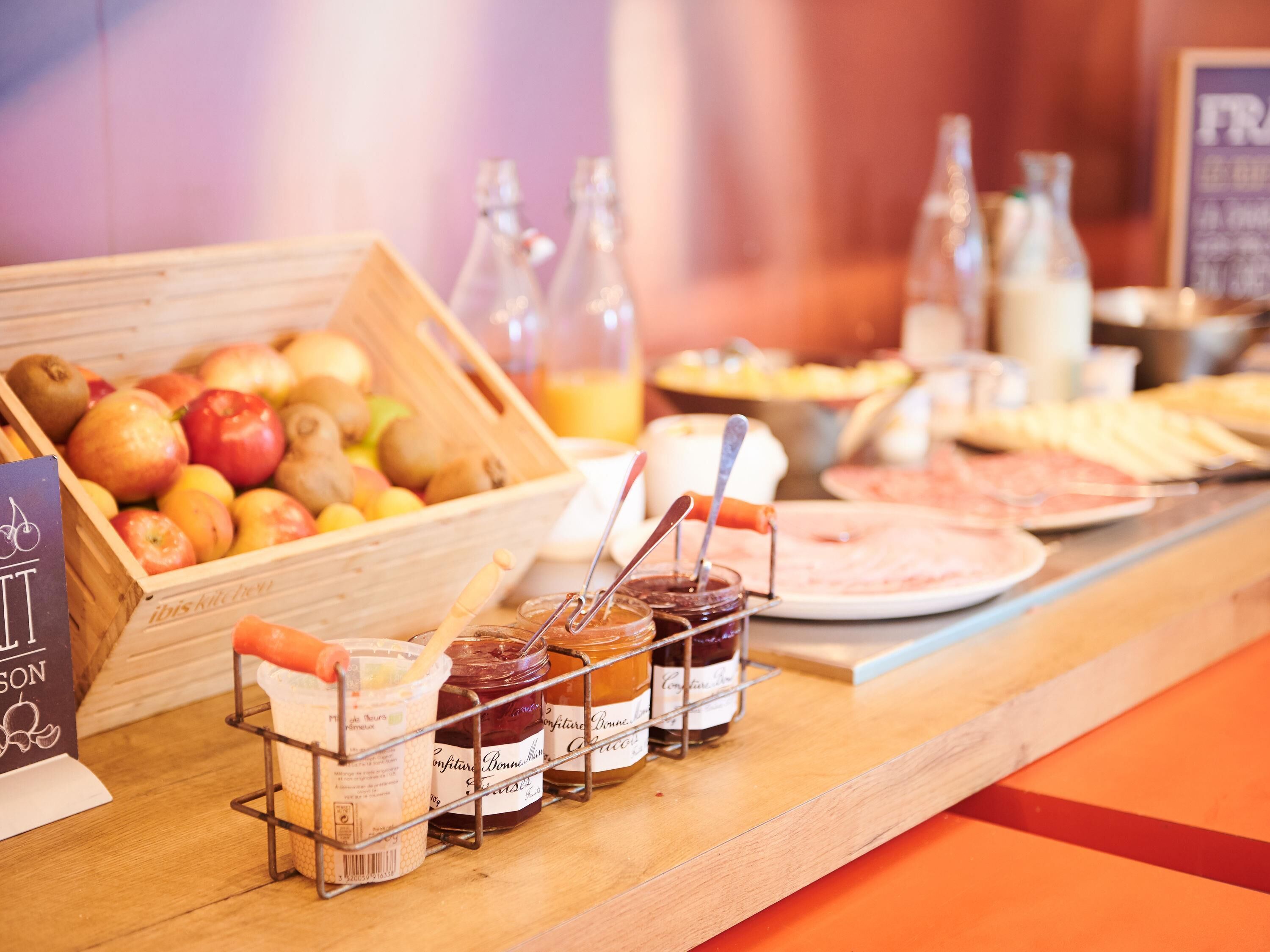 Un bufé de desayuno con frutas, mermeladas y un letrero que dice 'Ibis Kitchen'.