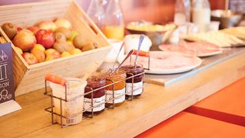 Un bufé de desayuno con frutas, mermeladas y un letrero que dice 'Ibis Kitchen'.
