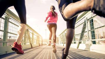 Un gruppo di persone corre su un ponte con ringhiere metalliche e palazzi sullo sfondo.