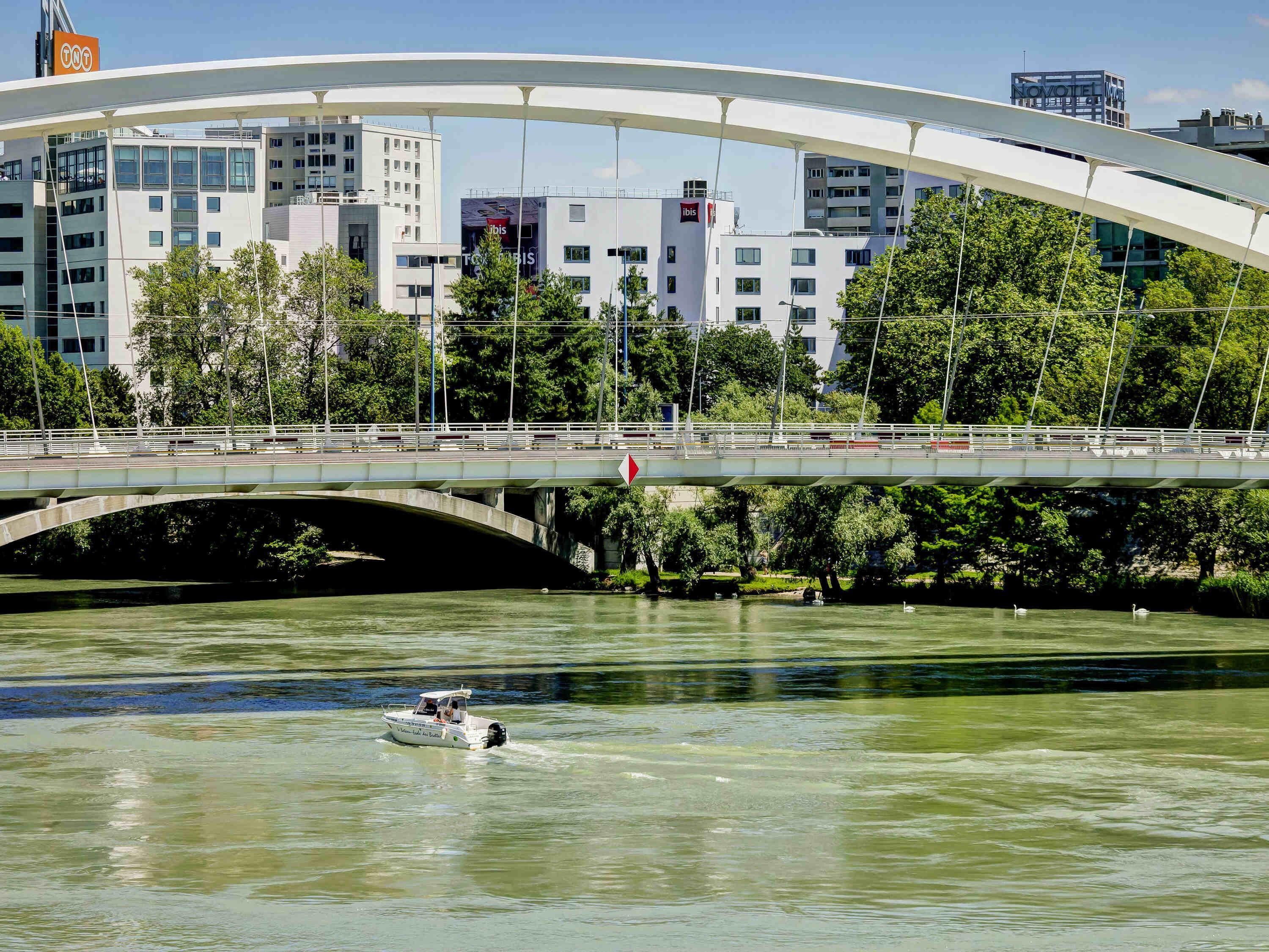 Un puente moderno con un arco blanco sobre un río, rodeado de edificios urbanos y vegetación.