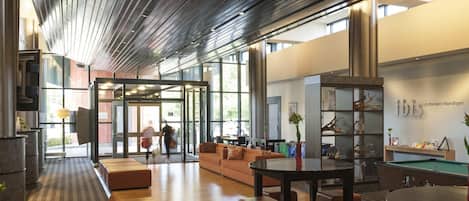 A modern lobby with a wooden ceiling, a pool table, and a seating area with sofas and chairs.