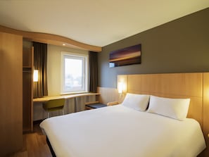 A hotel room with a large bed, a desk with a chair, a window, and a painting on the wall. - ibis Rotterdam Vlaardingen (Vlaardingen)