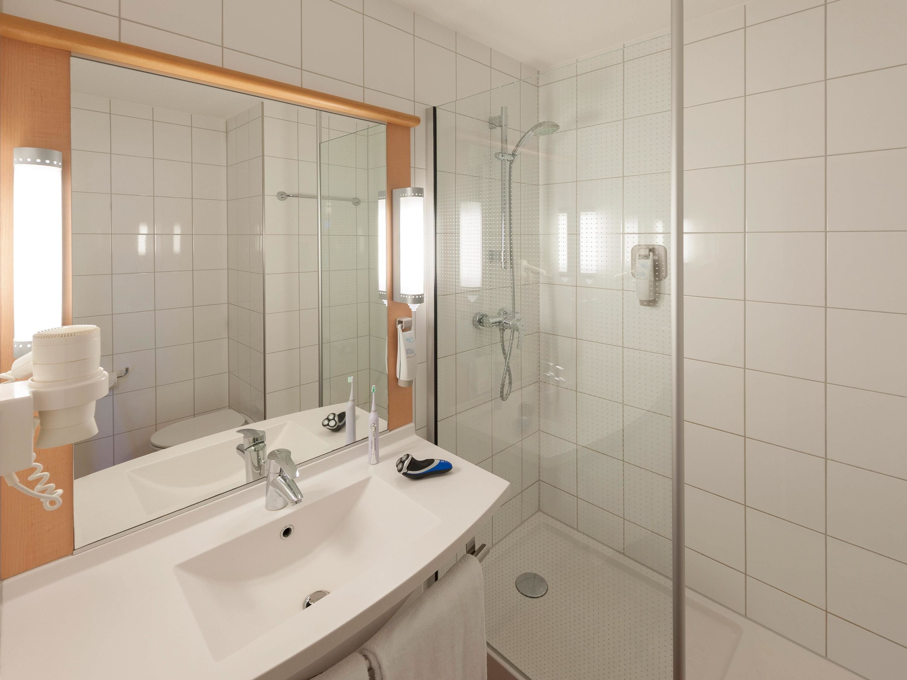 Une salle de bain moderne avec un lavabo blanc, un miroir et une douche séparée par une paroi de verre.