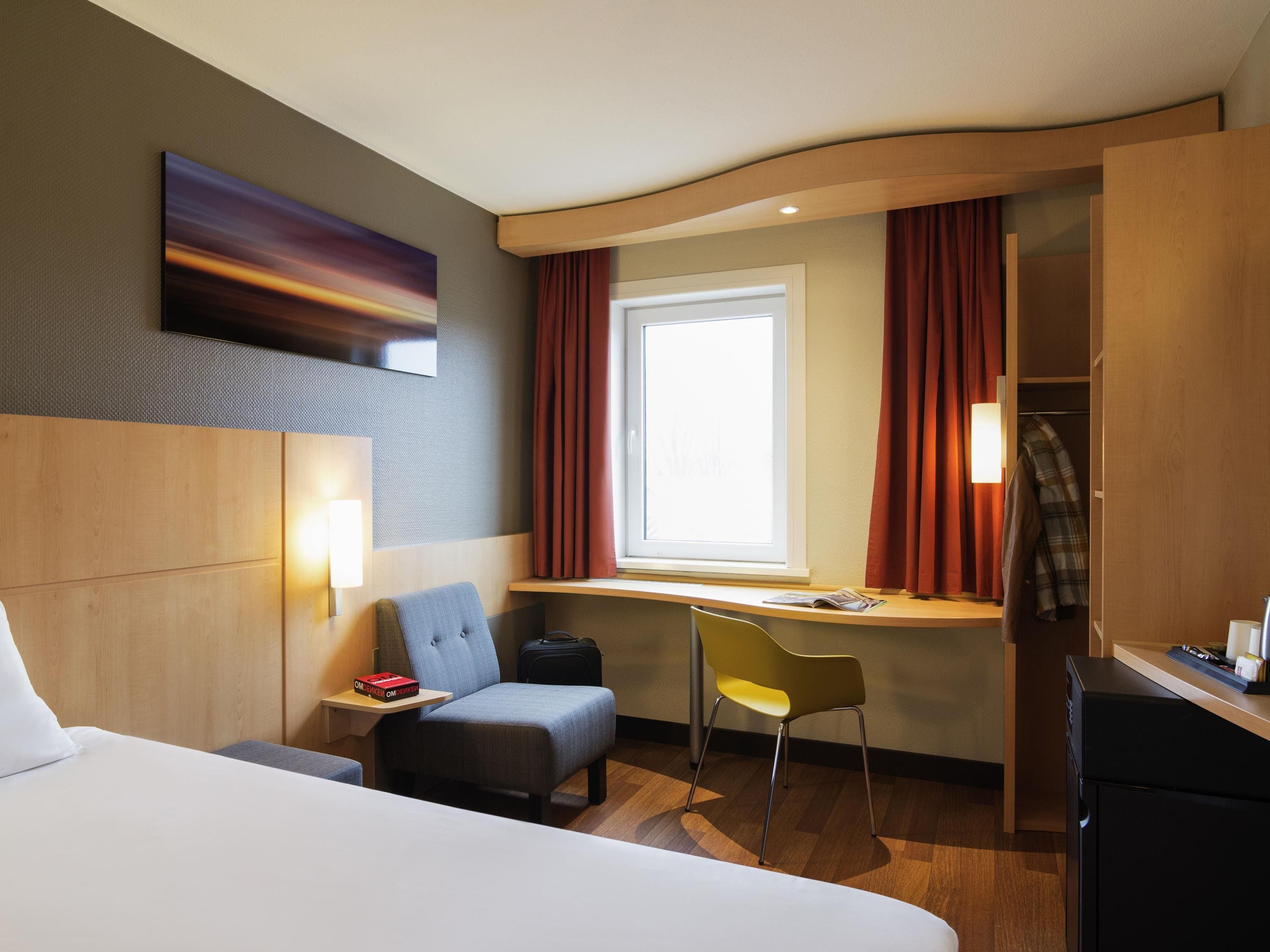 A hotel room with a bed, a desk, a chair, a TV, and a window with curtains.