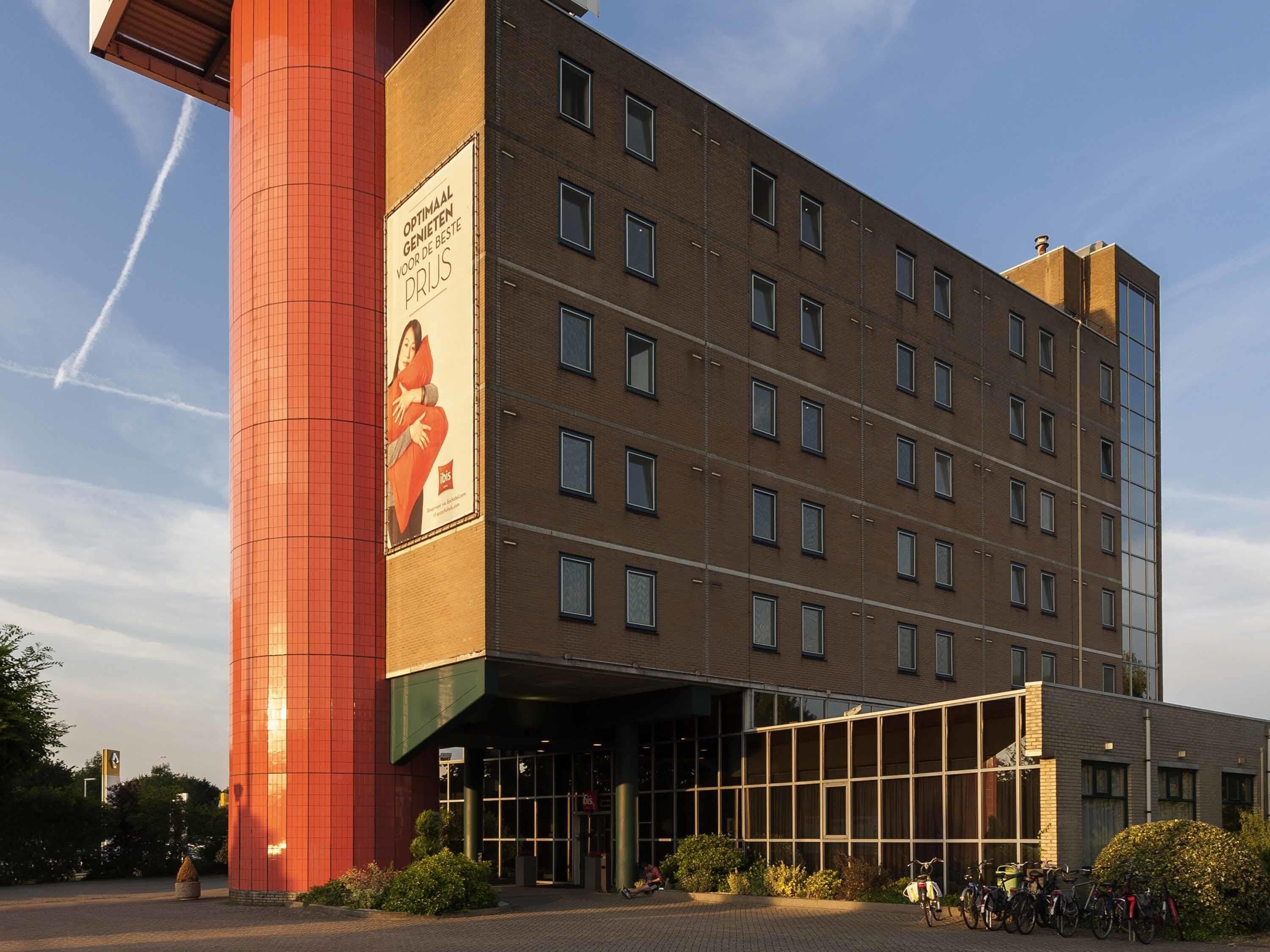 A multi-story hotel with a prominent red cylindrical structure on the left and a large glass entrance.