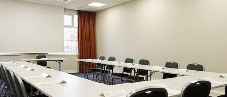 A conference room with a long table, chairs, a projector screen, and a window with curtains.