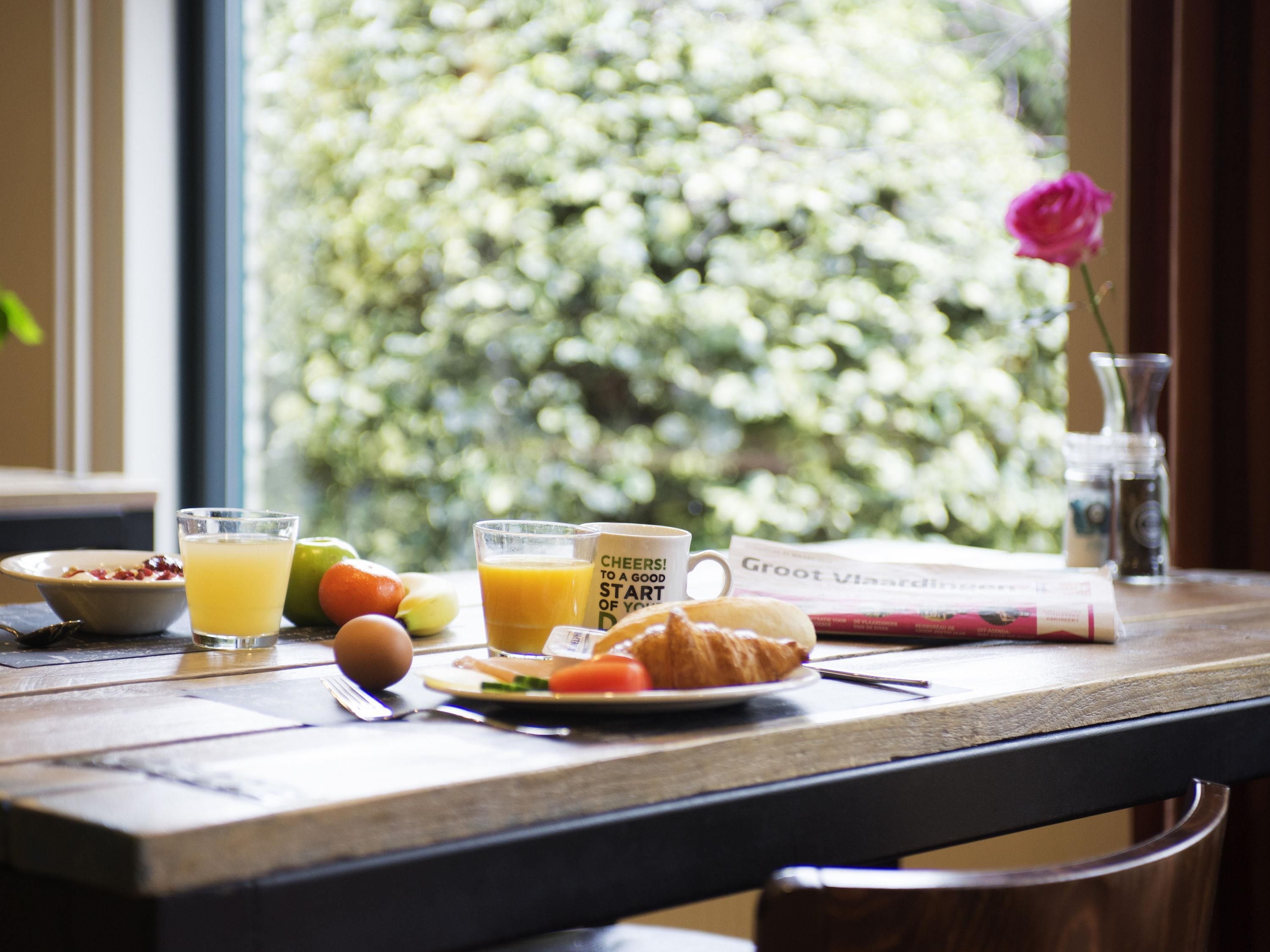 Una mesa de desayuno con un croissant, jugo de naranja, un bol de fruta y un periódico.