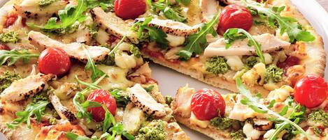 Una pizza con pollo, brócoli y tomates cherry sobre un plato blanco.