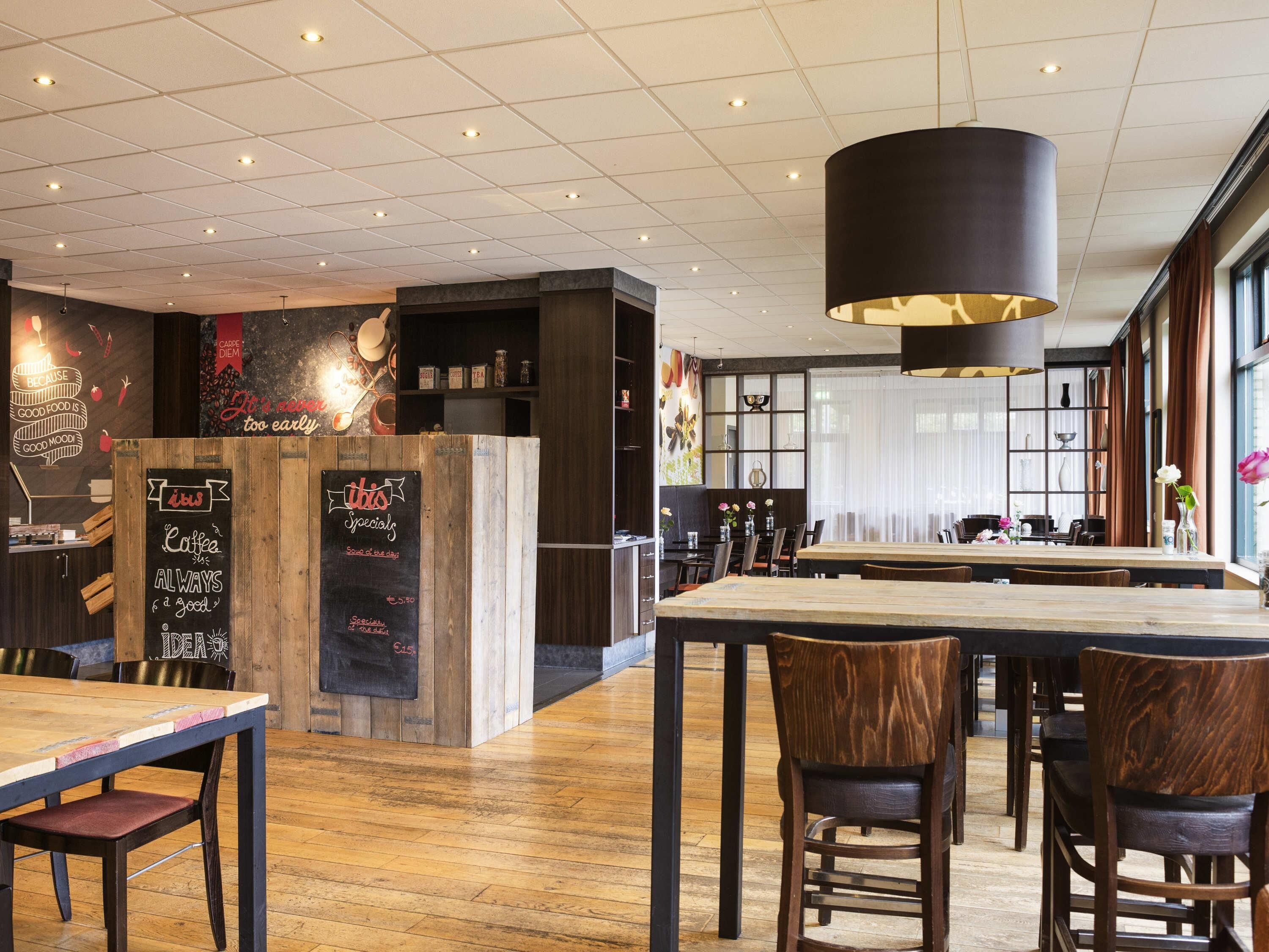 Interior de restaurante con suelo de madera, decoración en blanco y negro y una pizarra con el menú.