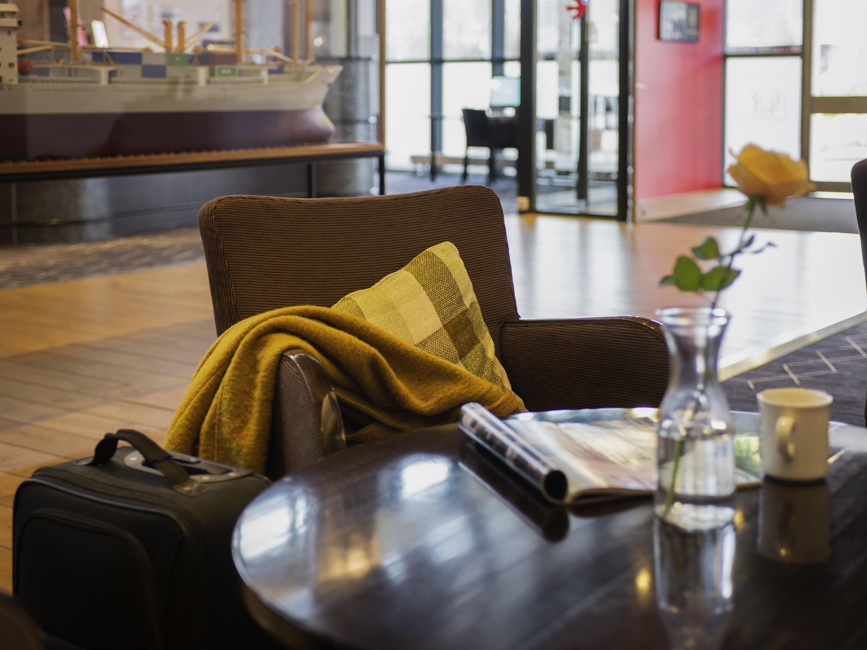 A hotel lobby with a wicker chair, a table with a vase, a ship model, and a rose.