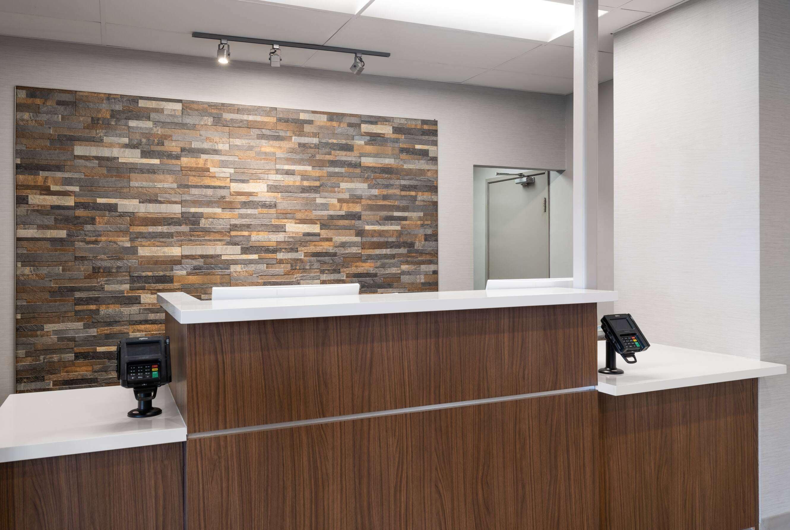A reception desk with a wooden finish, a stone-patterned wall, and a glass door in the background.