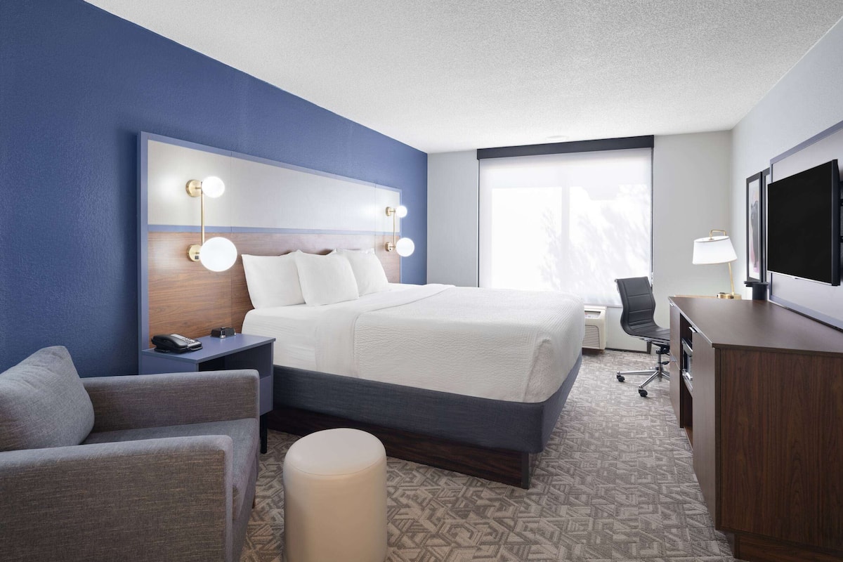 A hotel room with a large bed, bedside tables, a desk, a chair, and a TV.