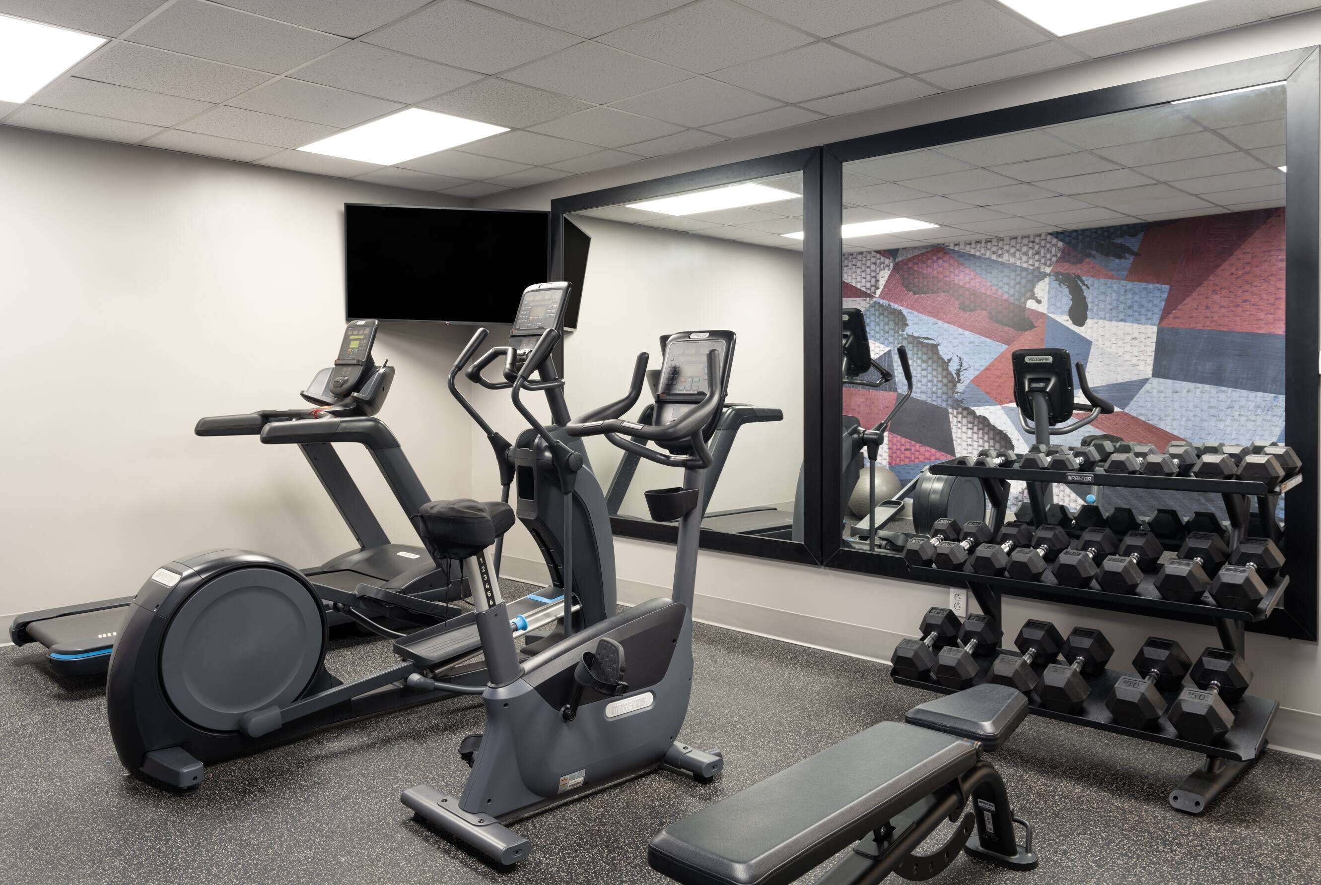 A gym with treadmills, an elliptical, a bench, and a rack of dumbbells.