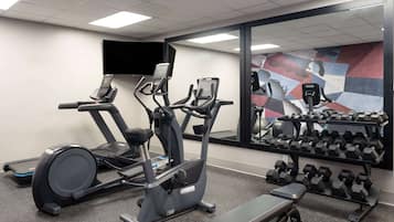 Een sportschool met loopbanden, een crosstrainer, een bank en een rek met gewichten.