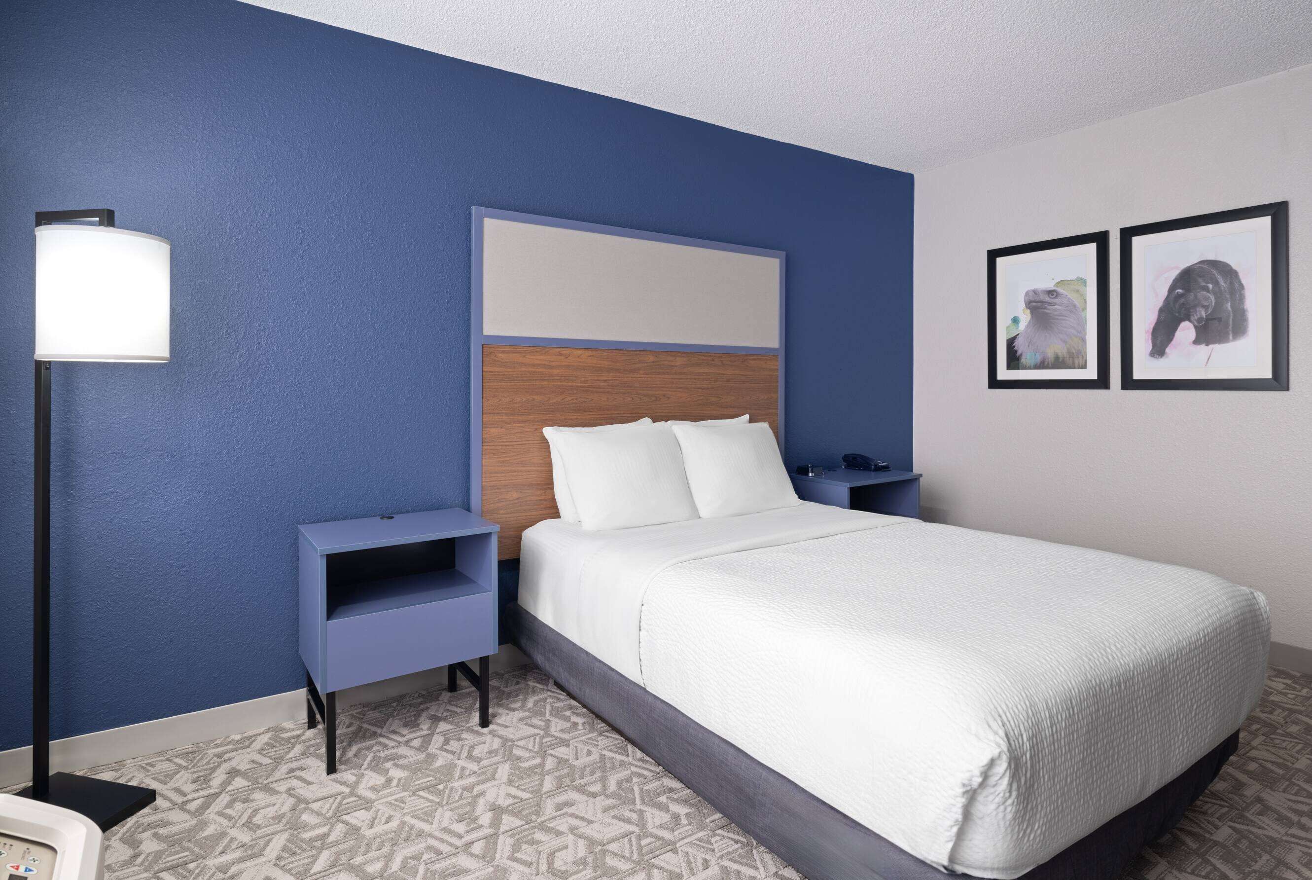 A neatly arranged hotel room with a bed, bedside tables, a lamp, and two framed pictures on the wall.