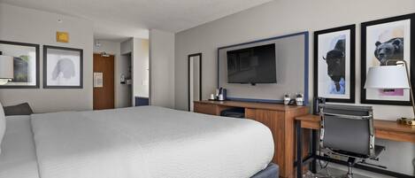 A hotel room with a large bed, a desk with a computer, a TV, and framed pictures on the wall.