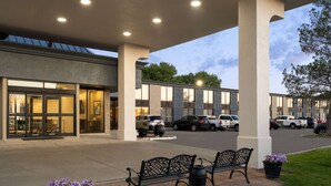 A hotel entrance with a covered walkway, outdoor seating, and a parking area.