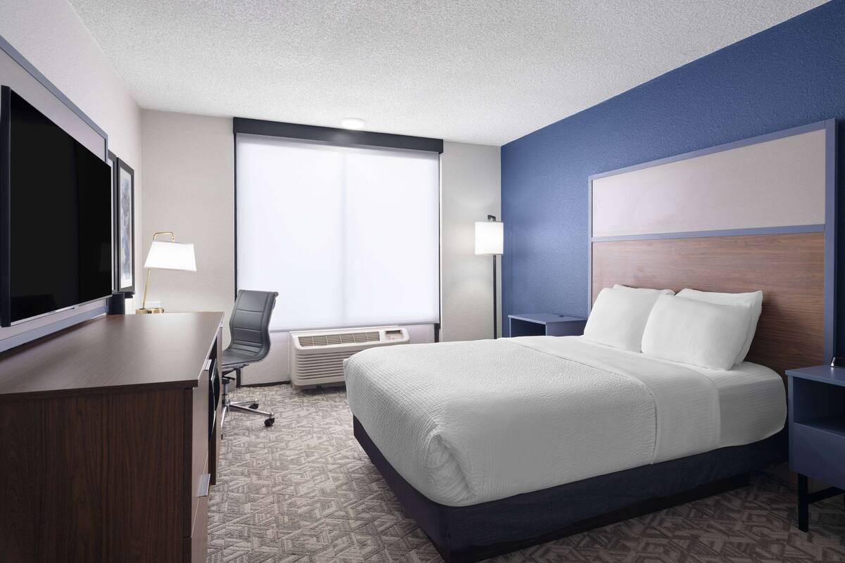 A hotel room with a bed, desk, chair, TV, and two bedside lamps.