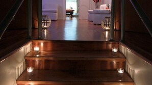 Un escalier en bois, illuminé de bougies, mène à un salon agrémenté d’un canapé et d’objets décoratifs.