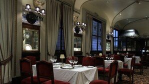 Une salle à manger avec des tables dressées pour le service, des chaises à revêtement rouge et des lustres.