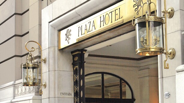 Une enseigne pour l’hôtel Plaza, avec des lettres dorées décorées et deux lanternes dorées de chaque côté.